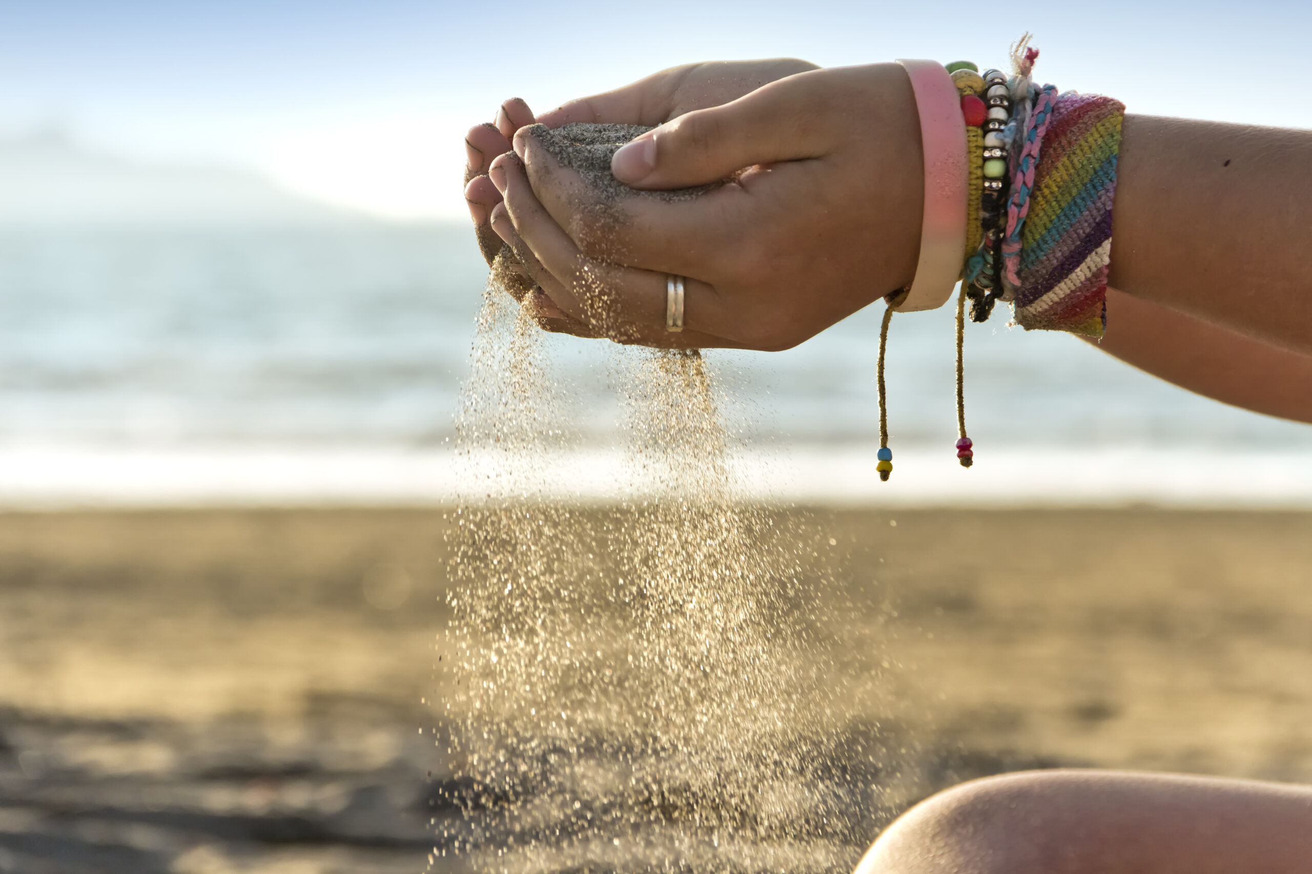 Beach sand, slips through the fingers of the hands of a young girl.