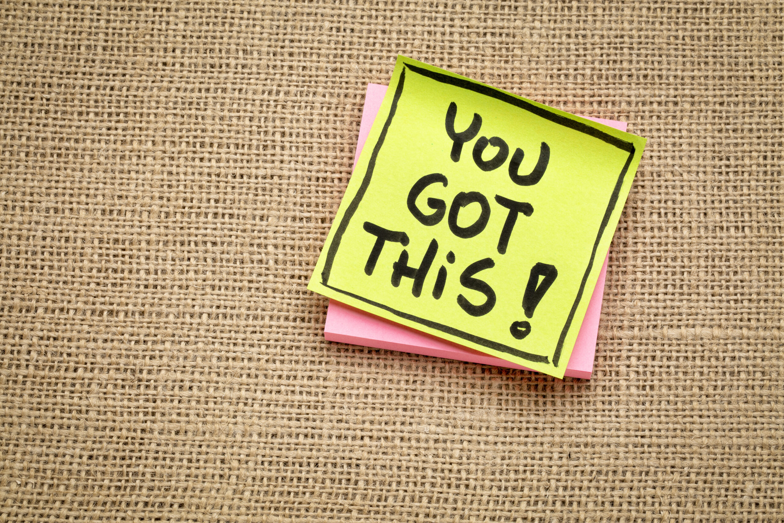 You got this! Handwriting on a sticky note against burlap canvas.