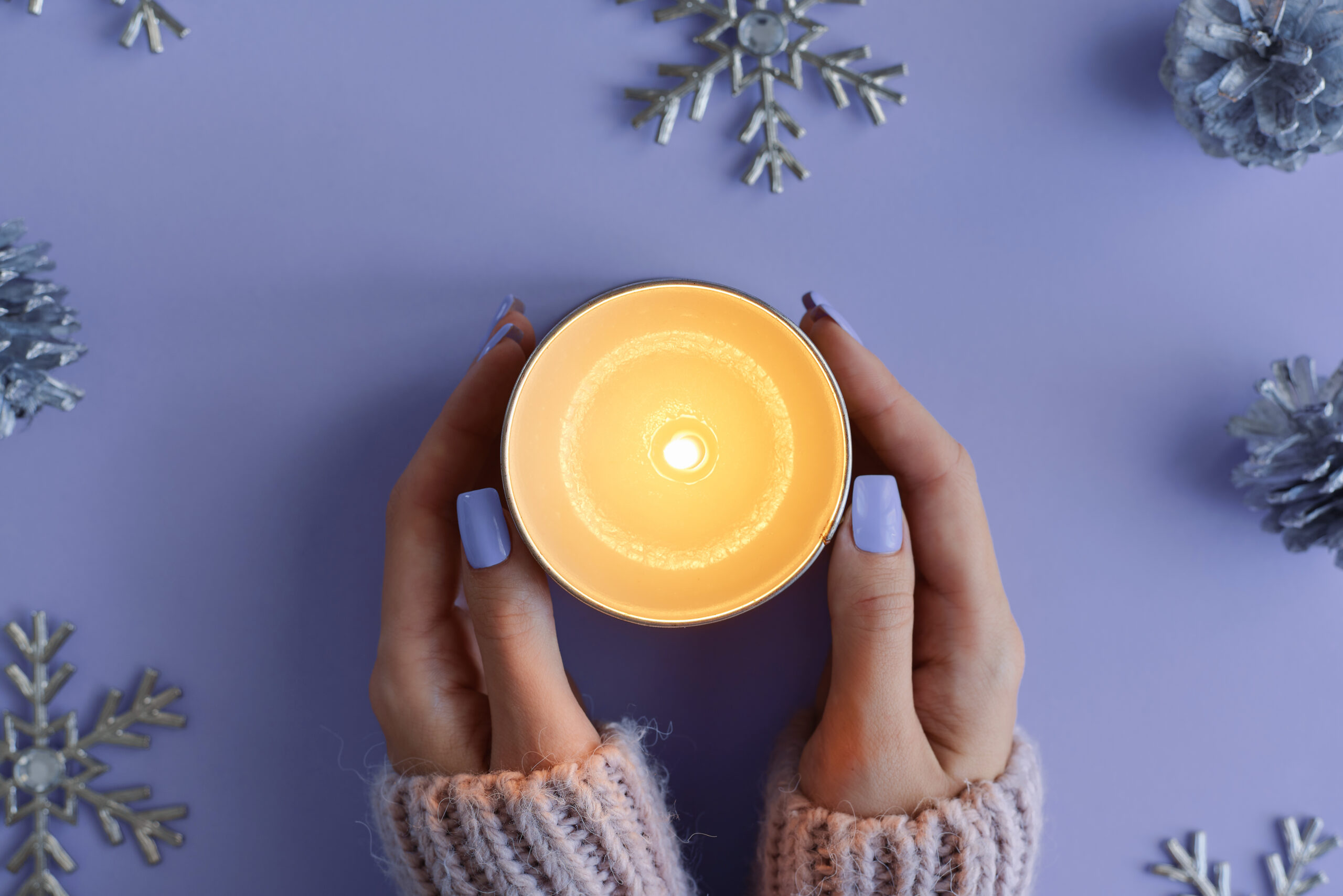 Female's hands with purple manicure holding a burning soy candle. Winter season concept, top view